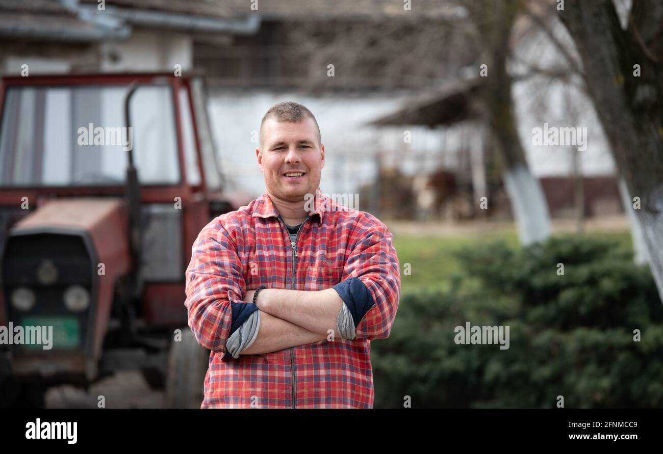 Éleveur heureux avec des bras croisés devant le tracteur à la ferme Banque D'Images