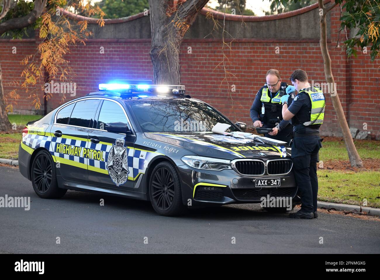 Une BMW M5 de patrouille routière de la police de Victoria, avec des feux clignotants, garée sur le côté de la route, tandis que deux policiers accomplissent leur travail Banque D'Images