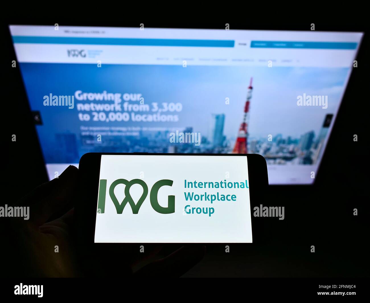 Personne détenant un smartphone avec le logo d'entreprise de la société internationale IWG plc sur l'écran devant la page Web. Mise au point sur l'affichage du téléphone. Banque D'Images