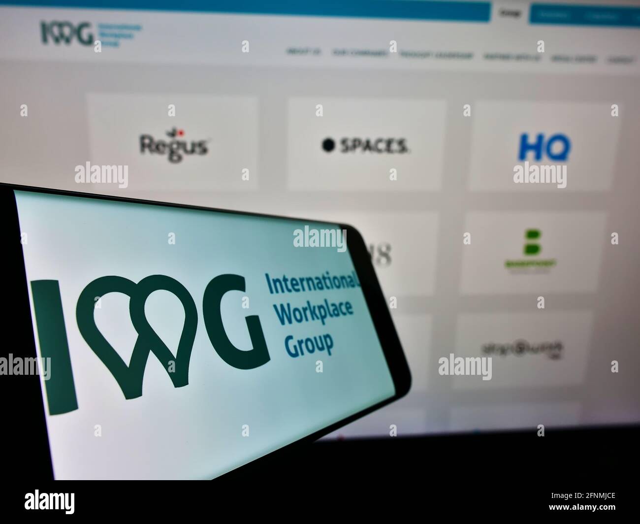 Téléphone mobile avec logo de la société multinationale de bureaux desservis IWG plc à l'écran devant la page Web. Mise au point au centre-gauche de l'écran du téléphone portable. Banque D'Images