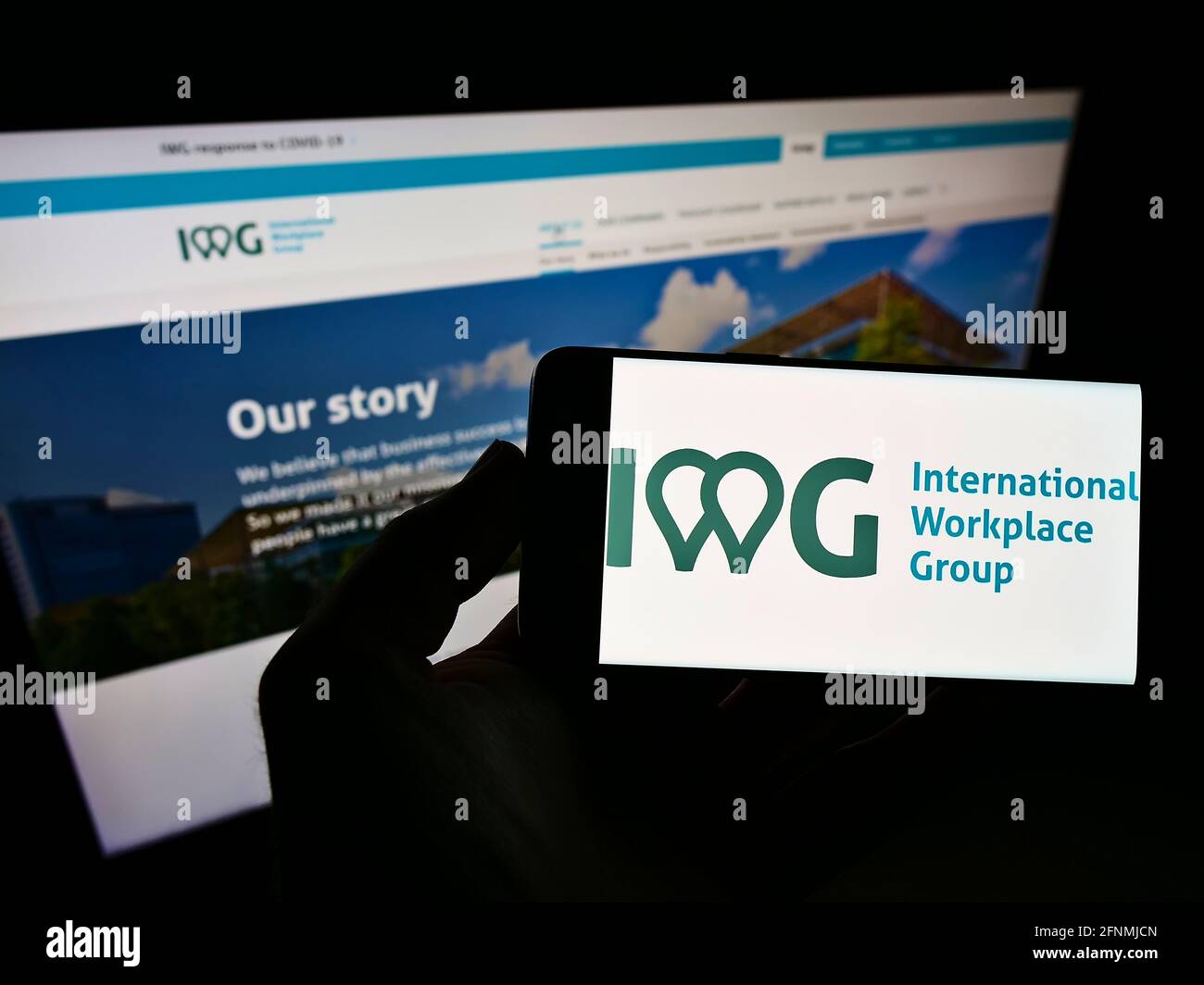 Personne détenant un smartphone avec le logo de la société multinationale de services IWG plc à l'écran devant le site Web. Mise au point sur l'affichage du téléphone. Banque D'Images