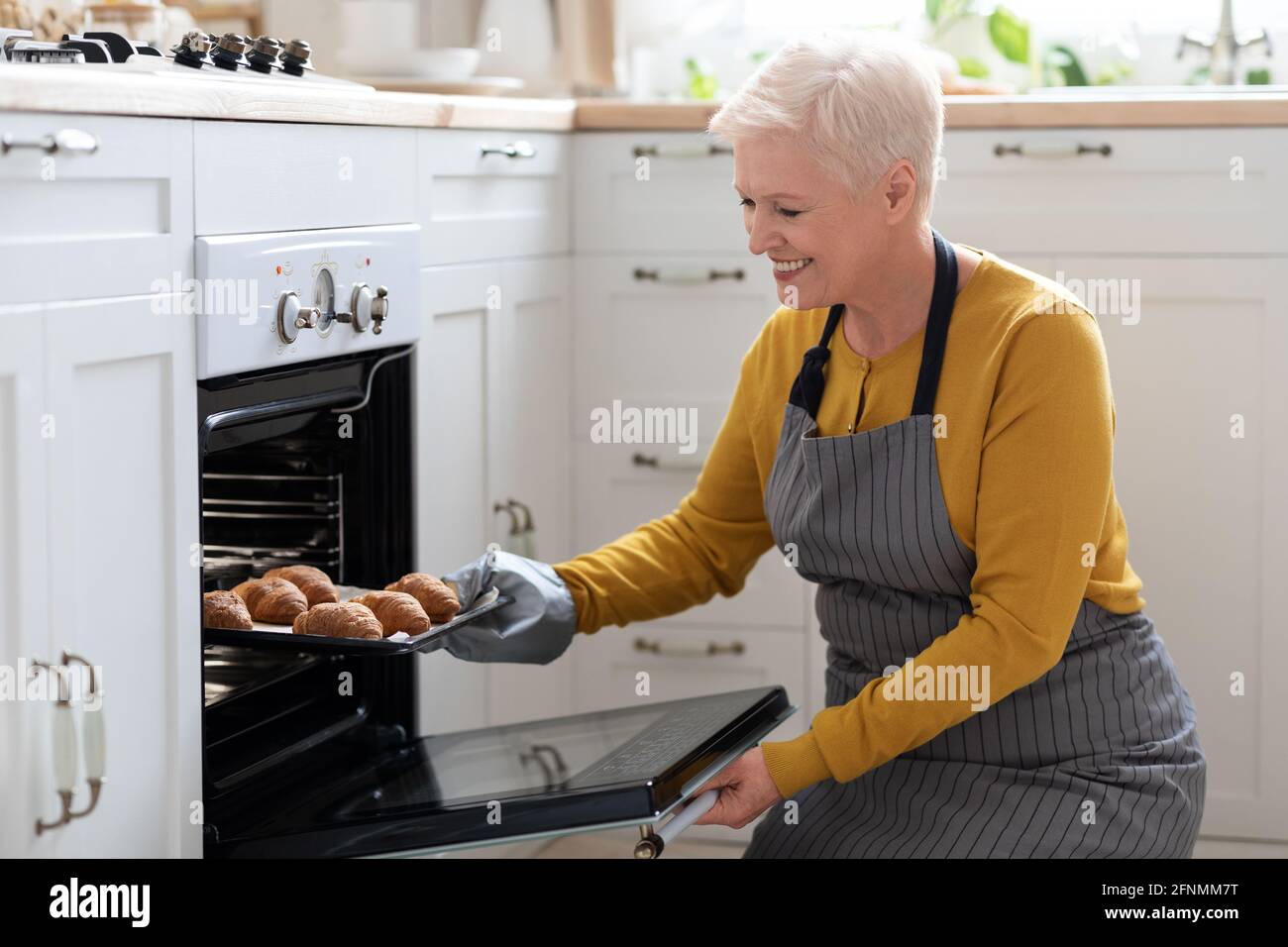 Femme âgée souriante prenant des croissants au four Banque D'Images