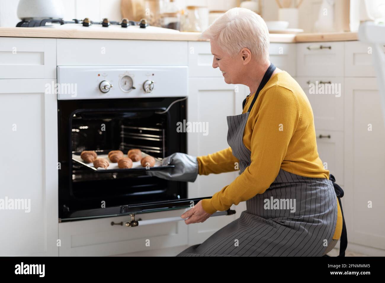 Grand-mère joyeuse prenant des croissants faits maison au four Banque D'Images