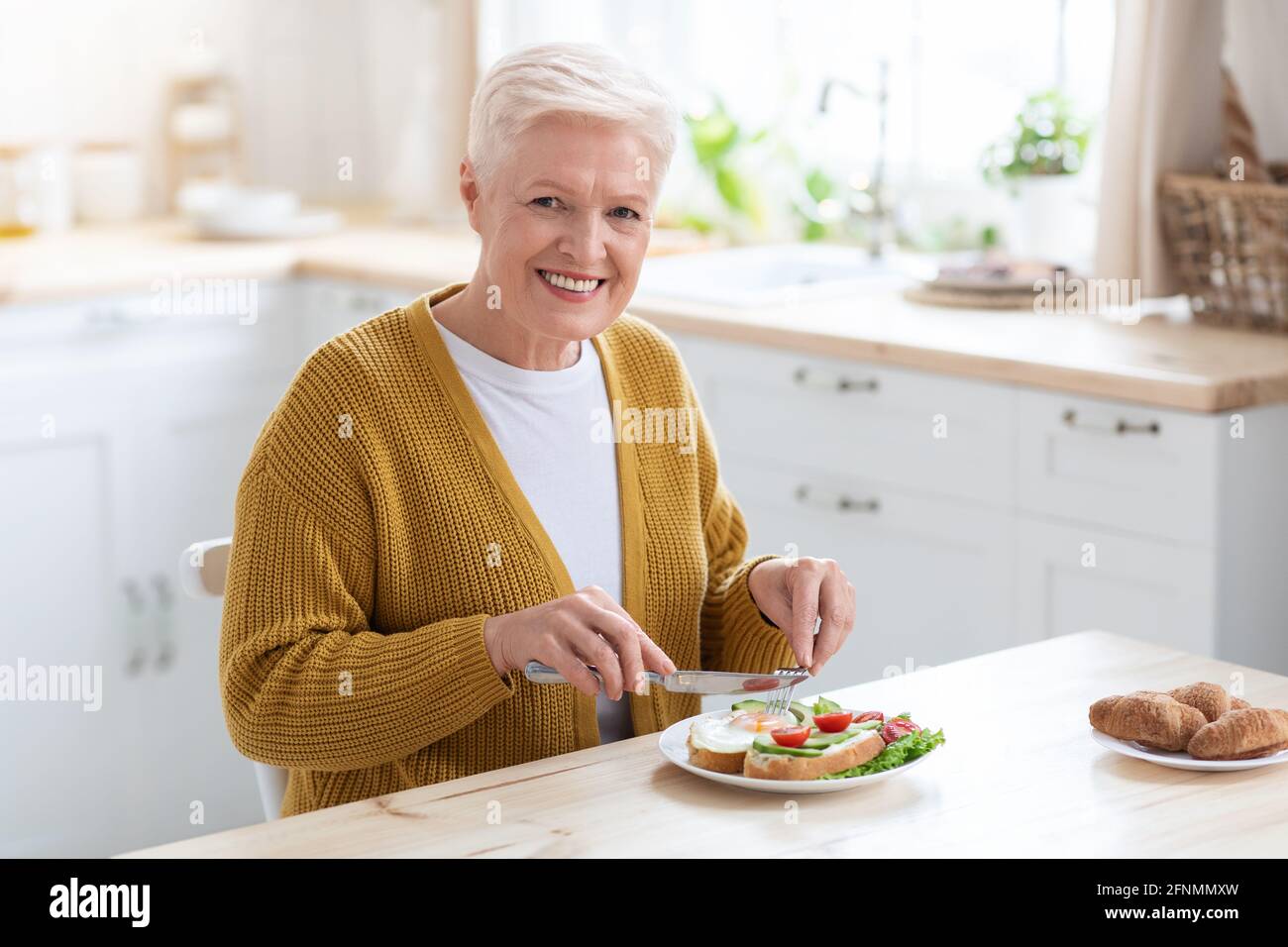 Une femme âgée en bonne santé et gaie qui apprécie son déjeuner à la maison Banque D'Images