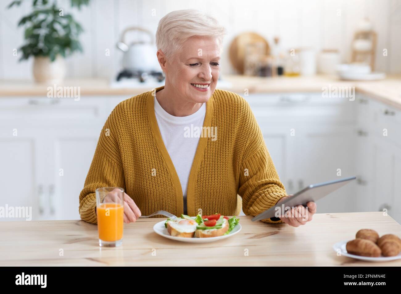 Femme sénior ayant déjeuné et utilisant une tablette numérique Banque D'Images