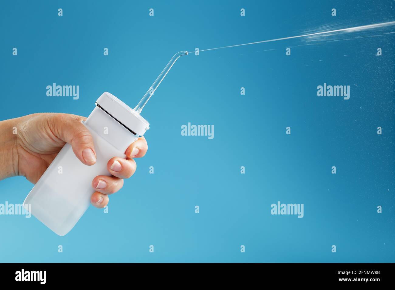 Irrigateur en main pour nettoyer la bouche avec un jet d'eau sur fond bleu. Un appareil mobile pour se brosser les dents et un sourire blanc neige Banque D'Images