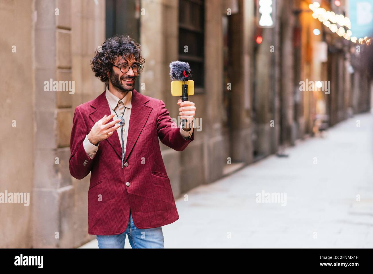 Charmant homme caucasien s'enregistrant dans les rues de Barcelone. Il tient une nacelle avec un téléphone mobile jaune et un microphone. Il est dres Banque D'Images