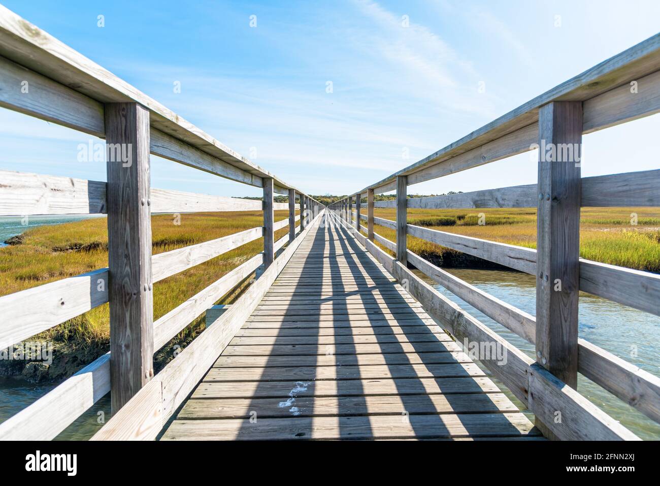 Vue à angle bas d'une passerelle clôturée déserte à travers le marais d'eau salée lors d'une journée d'automne ensoleillée. Lignes convergentes Banque D'Images