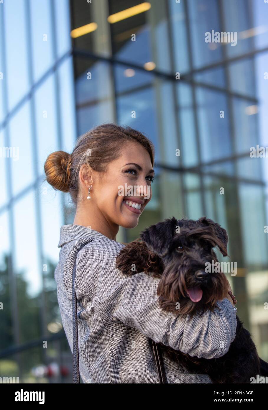 Jolie jeune femme d'affaires tenant un chien mignon dans les bras devant le bâtiment des bureaux Banque D'Images
