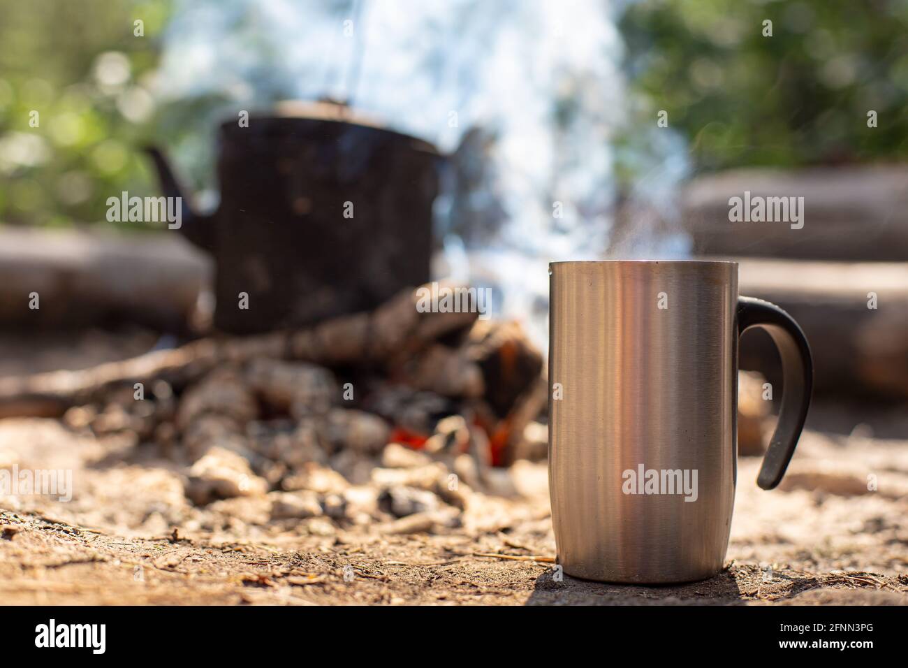 Une tasse en métal avec une boisson chaude se tient sur le sol, sur fond  d'un feu de camp avec une bouilloire, sur une randonnée, dans la forêt  Photo Stock - Alamy