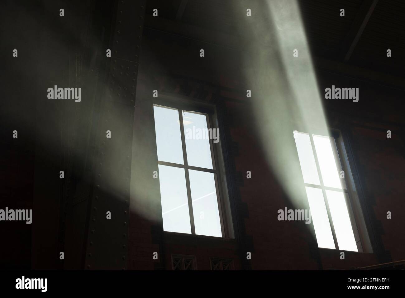 Des rayons de soleil se diffusent à travers les fenêtres d'un grand bâtiment ancien. L'atmosphère intérieure poussiéreuse a créé ces poutres frappantes Banque D'Images