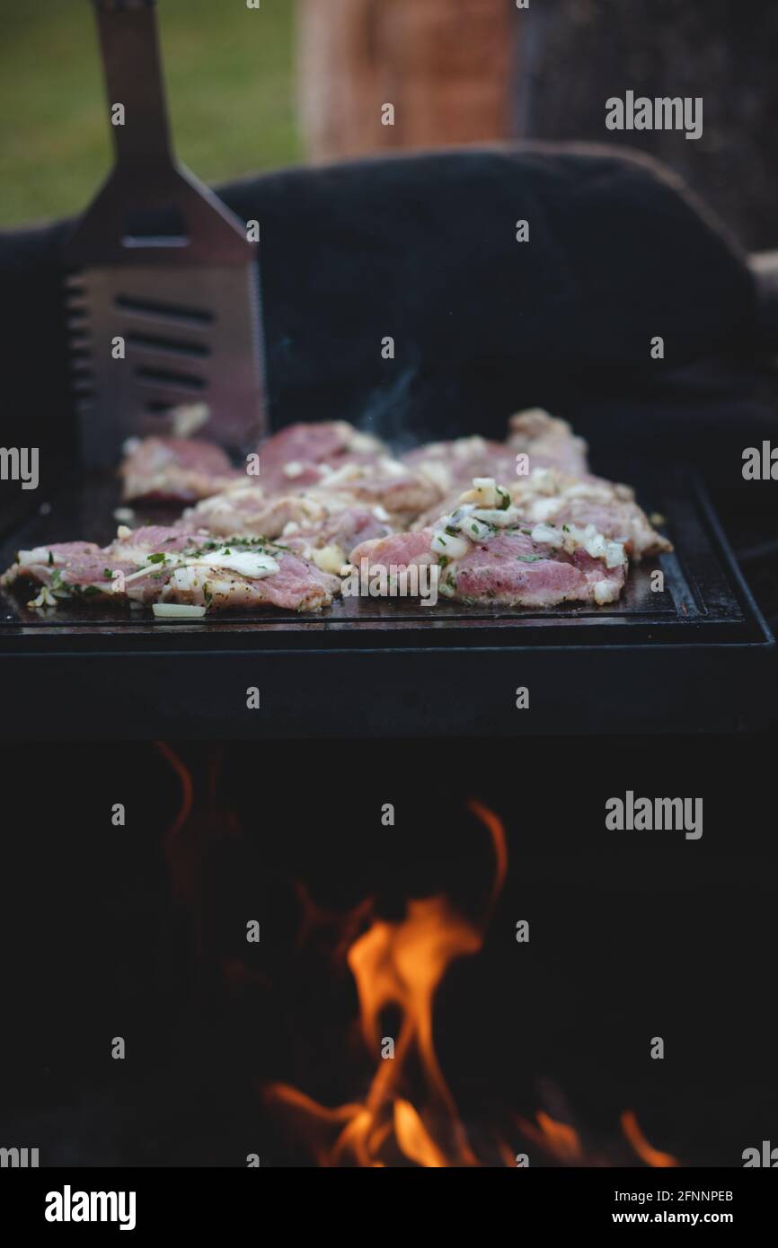 L'homme utilise une louche en acier pour tourner un col de porc chargé avec du basilic, du sel, du poivre et de l'huile d'un côté à l'autre. Barbecue sur un sapin extérieur féroce Banque D'Images