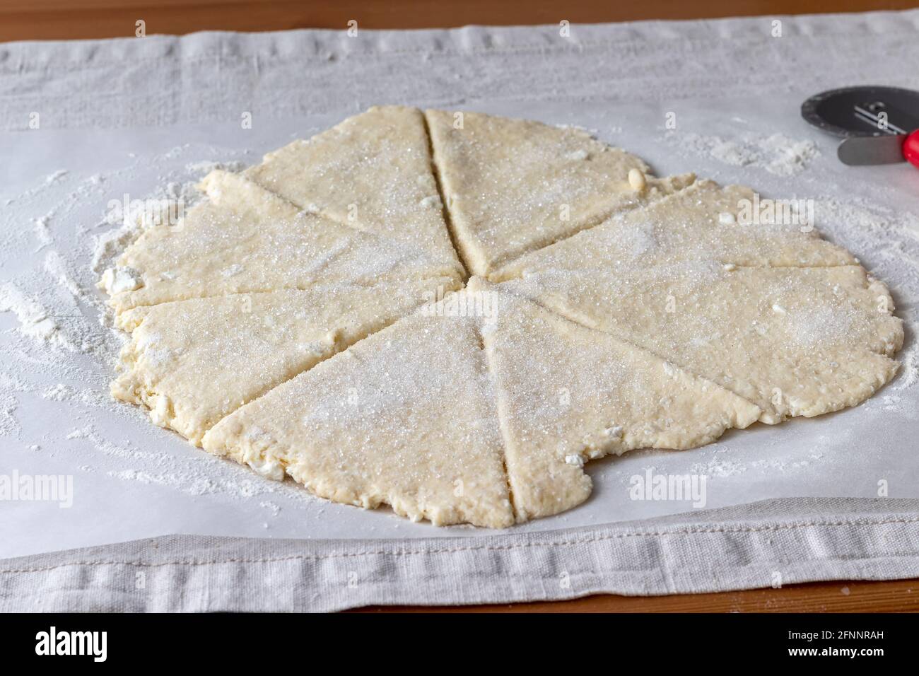 Pâte de caillé brute roulée avec morceaux de fromage cottage coupés en huit triangles parsemés de sucre sur du papier à pâtisserie une nappe en lin sur un tabl en bois Banque D'Images