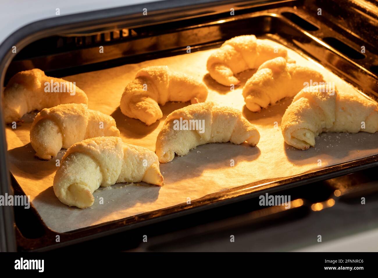 Croissants à sucre dépoli cuits au four sur une plaque de cuisson  recouverte de papier parchemin. Petits pains sucrés d'une pâte au fromage  cottage cuite dans un four chaud. Le Photo Stock -