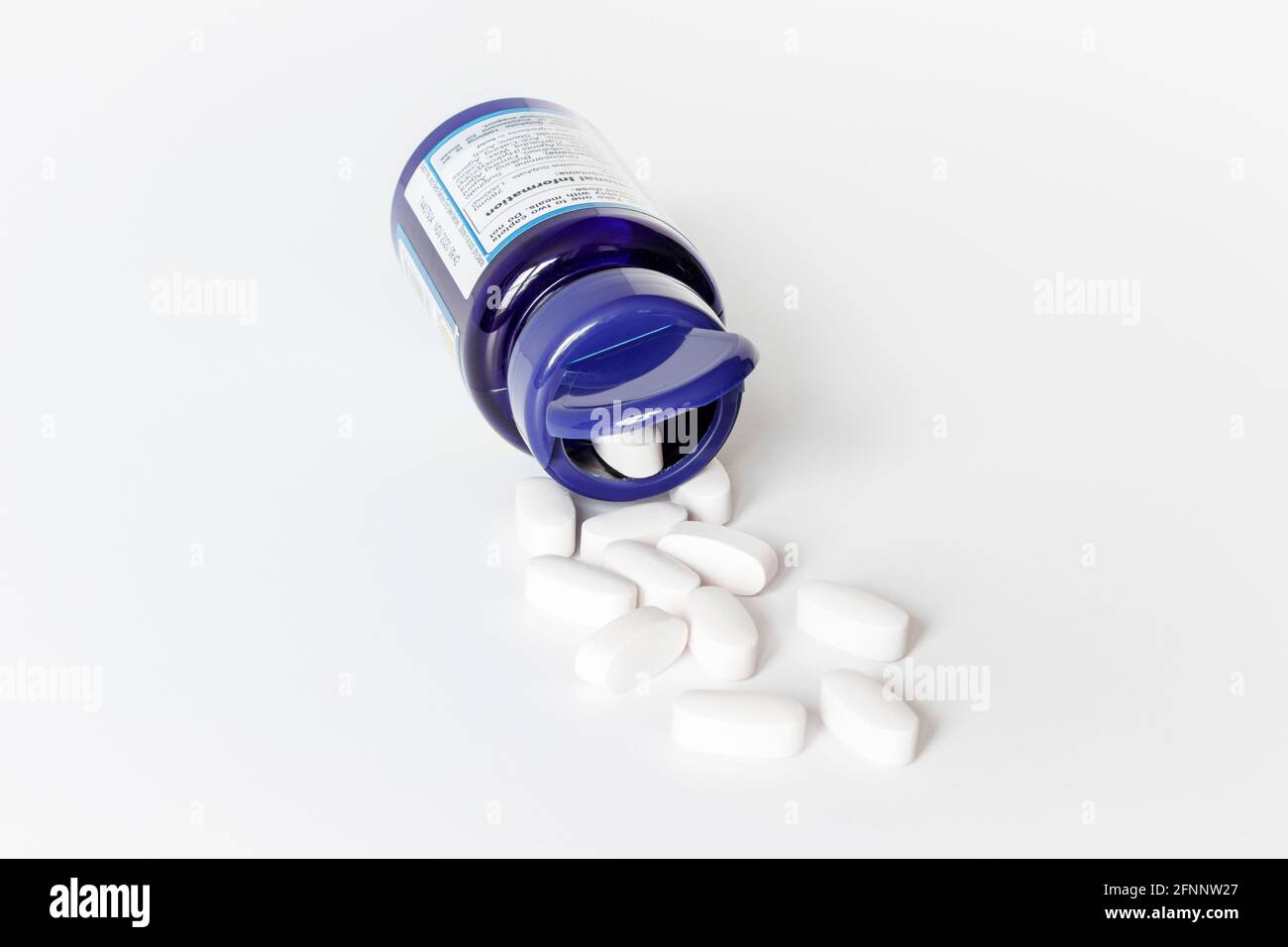 Les comprimés de sulfate de glucosamine blanc débordent d'un bleu ouvert conteneur en plastique sur fond blanc Banque D'Images