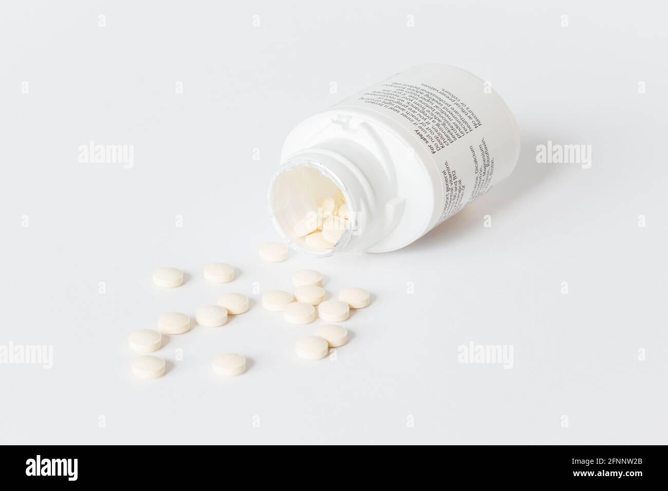 Des comprimés de vitamine débordent d'un récipient en plastique ouvert sur un arrière-plan blanc Banque D'Images