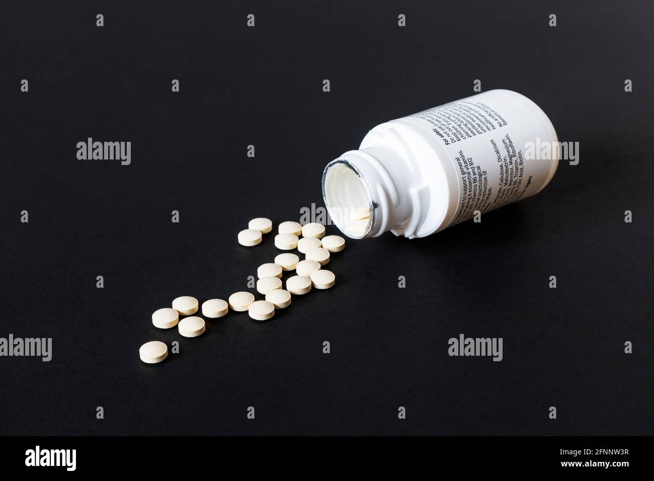 Des comprimés de vitamine sortent d'un récipient en plastique blanc ouvert sur fond noir Banque D'Images