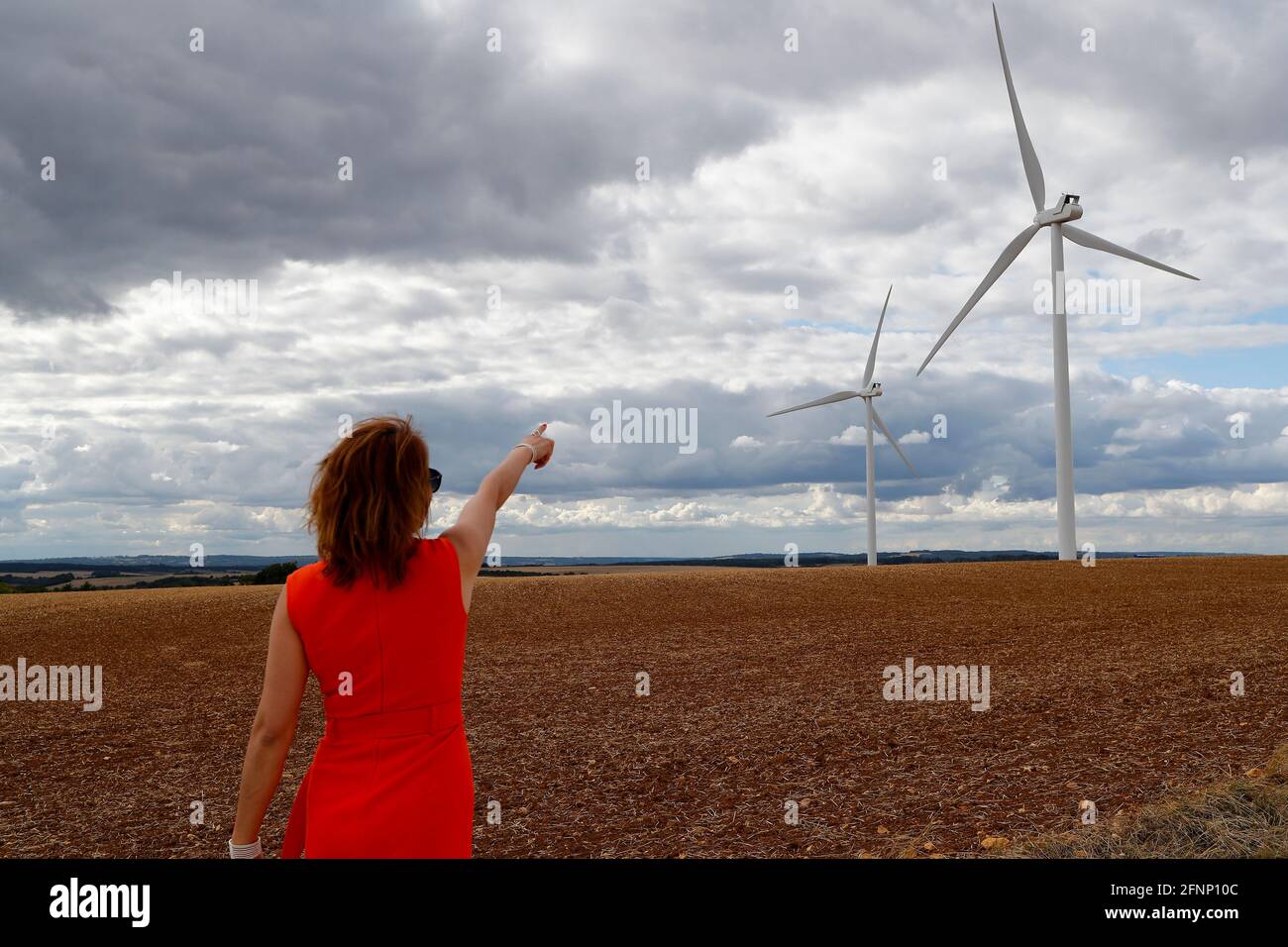 Femme montrant l'éolienne dans les champs. Ciel nuageux. France. Banque D'Images