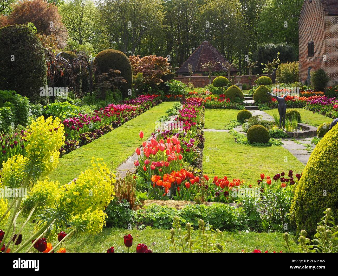 Chenies Manor jardin en contrebas dans la lumière de la fin de l'après-midi, orienté vers l'ouest. L'ancien pavillon restauré est un décor de tulipes colorées d'orange, de rouge et de pourpre. Banque D'Images