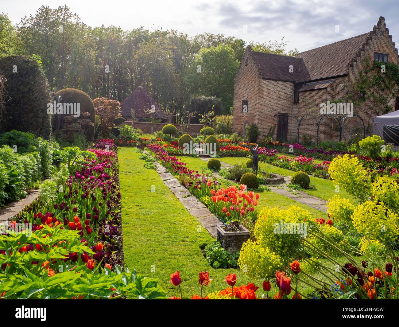 Chenies Manor jardin en contrebas dans la lumière de la fin de l'après-midi, orienté vers l'ouest. L'ancien pavillon restauré est un décor de tulipes colorées d'orange, de rouge et de pourpre. Banque D'Images