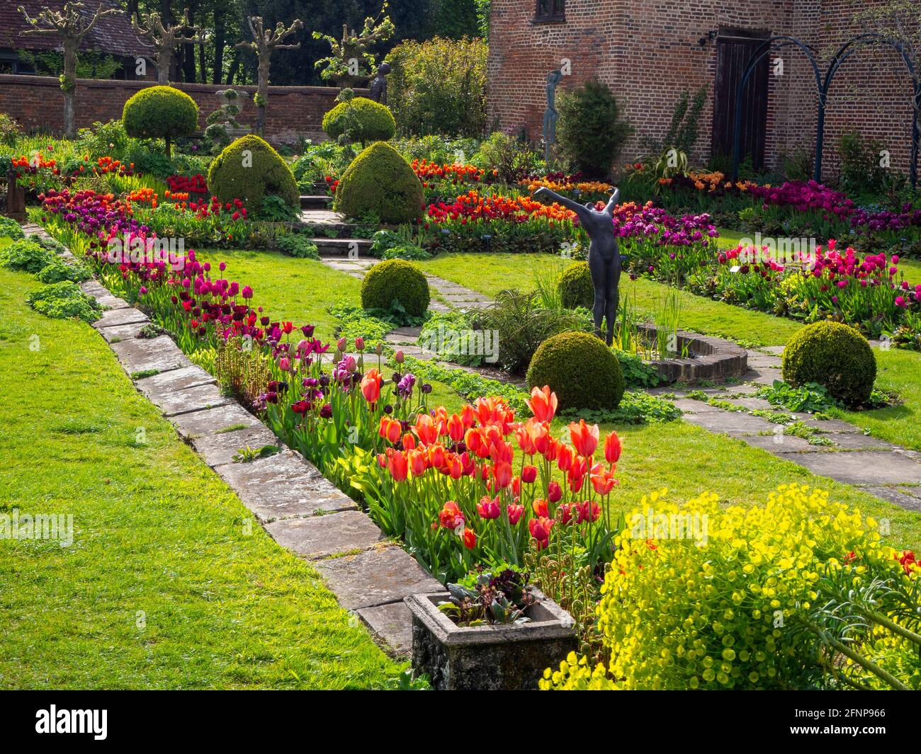 Chenies Manor jardin en contrebas dans la lumière de la fin de l'après-midi, orienté vers l'ouest. L'ancien pavillon restauré est un décor de tulipes colorées d'orange, de rouge et de pourpre. Banque D'Images