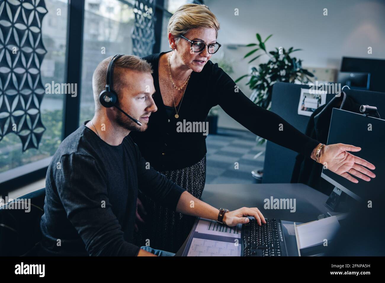 Femme professionnelle pointant sur l'écran d'ordinateur et discutant d'un problème avec un homme travaillant à son bureau. Responsable assistant l'agent du service client à la reso Banque D'Images