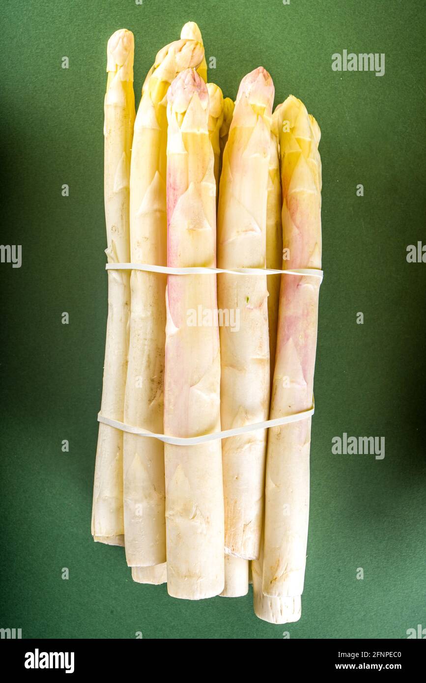 Bouquet d'asperges fraîches, crues, légumes violets, verts et blancs sur fond vert foncé Banque D'Images