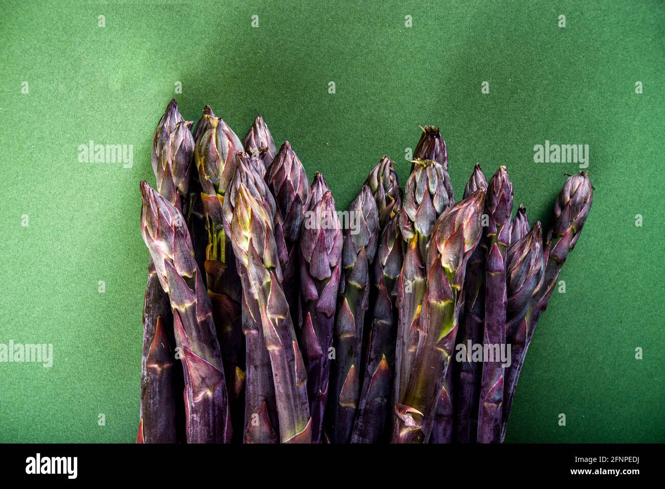 Bouquet d'asperges fraîches, crues, légumes violets, verts et blancs sur fond vert foncé Banque D'Images