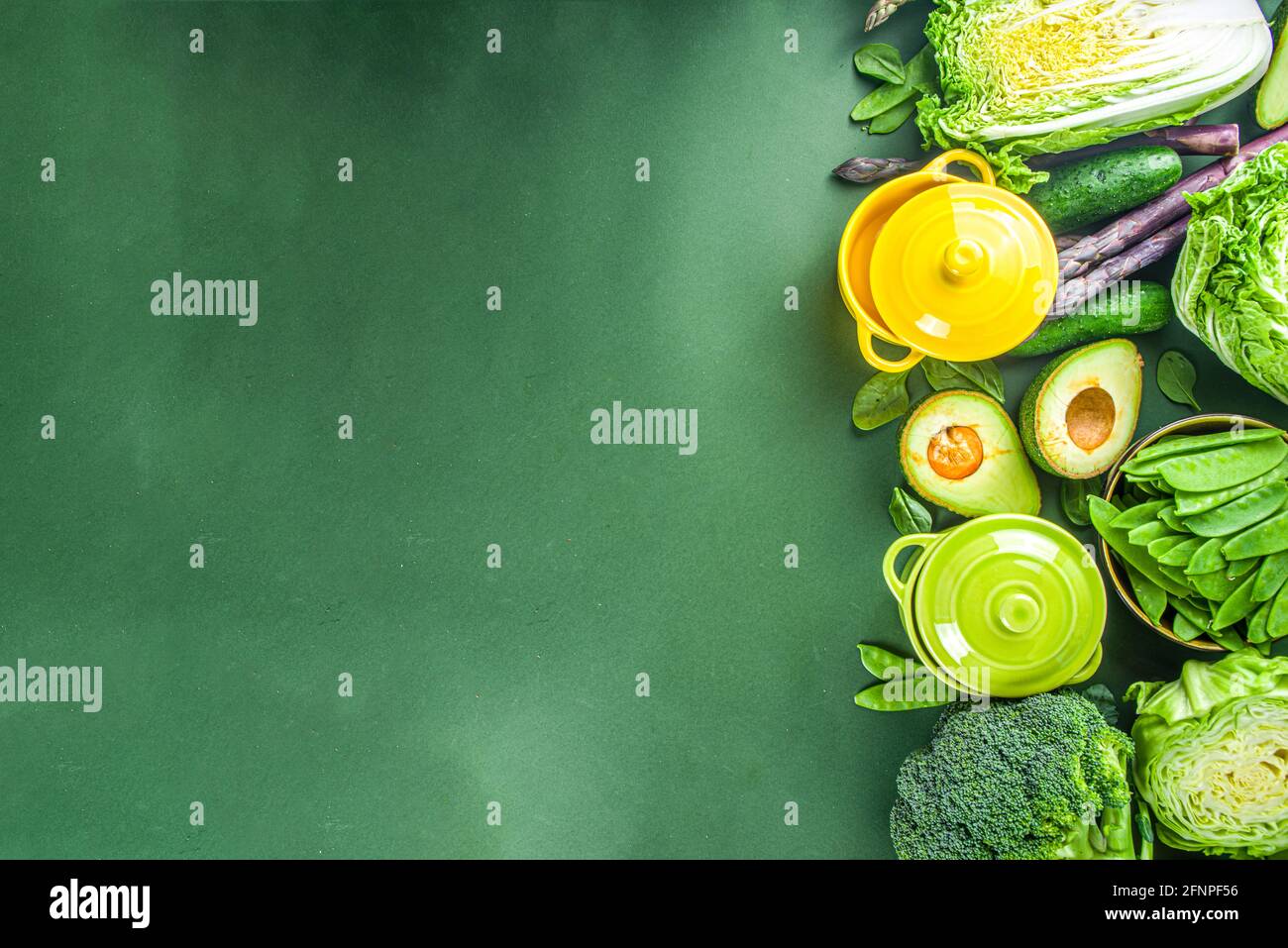 Divers ingrédients biologiques de légumes de printemps verts avec des marmites colorées vides sur table de cuisine vert foncé, vue du dessus. Une soupe saine à l'alimentation Banque D'Images