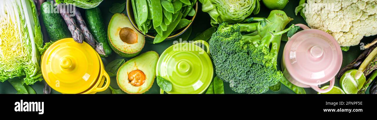 Divers ingrédients biologiques de légumes de printemps verts avec des marmites colorées vides sur table de cuisine vert foncé, vue du dessus. Une soupe saine à l'alimentation Banque D'Images
