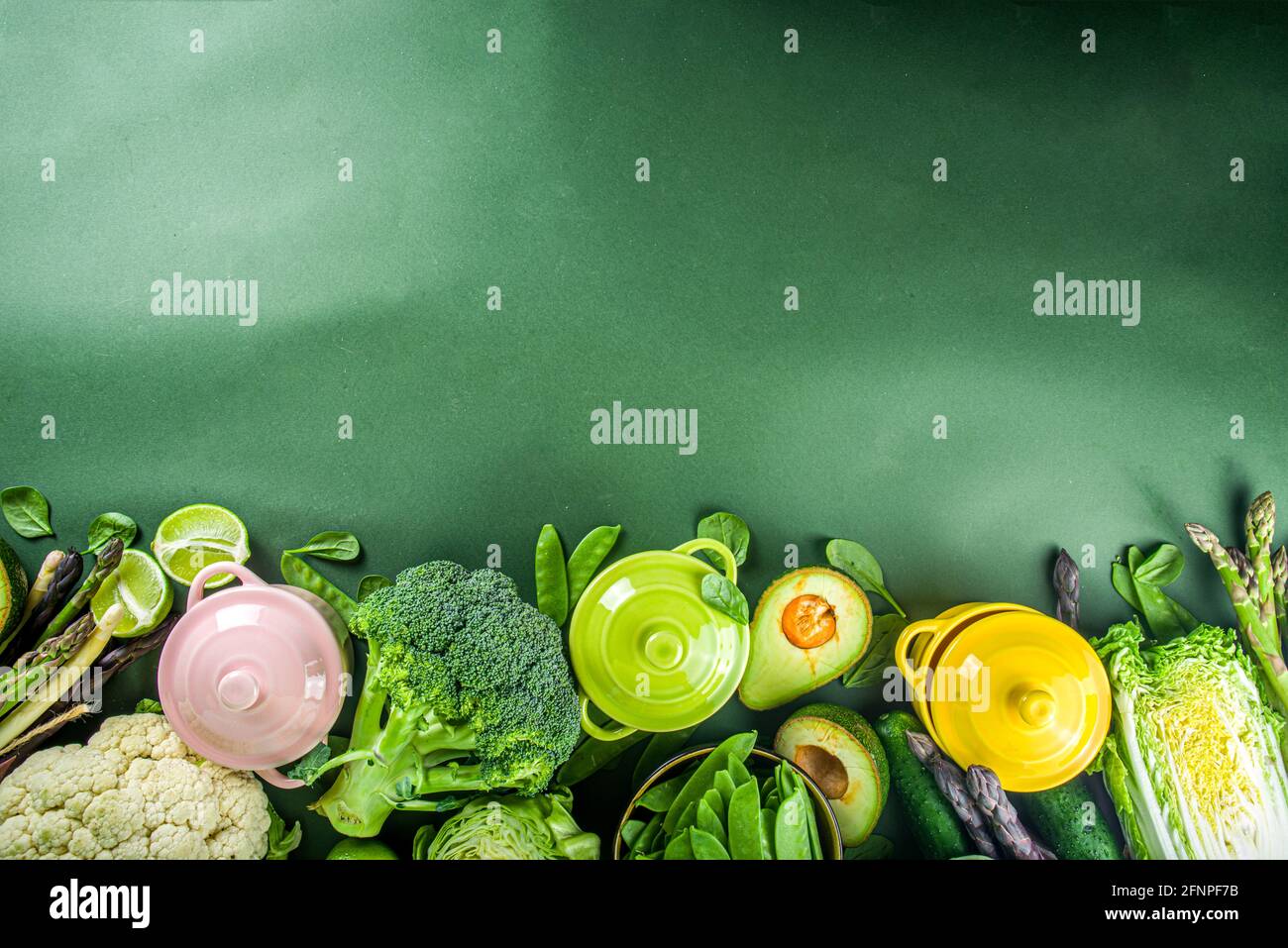 Divers ingrédients biologiques de légumes de printemps verts avec des marmites colorées vides sur table de cuisine vert foncé, vue du dessus. Une soupe saine à l'alimentation Banque D'Images