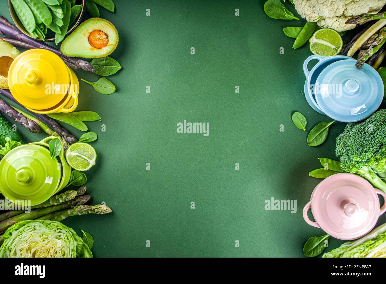 Divers ingrédients biologiques de légumes de printemps verts avec des marmites colorées vides sur table de cuisine vert foncé, vue du dessus. Une soupe saine à l'alimentation Banque D'Images