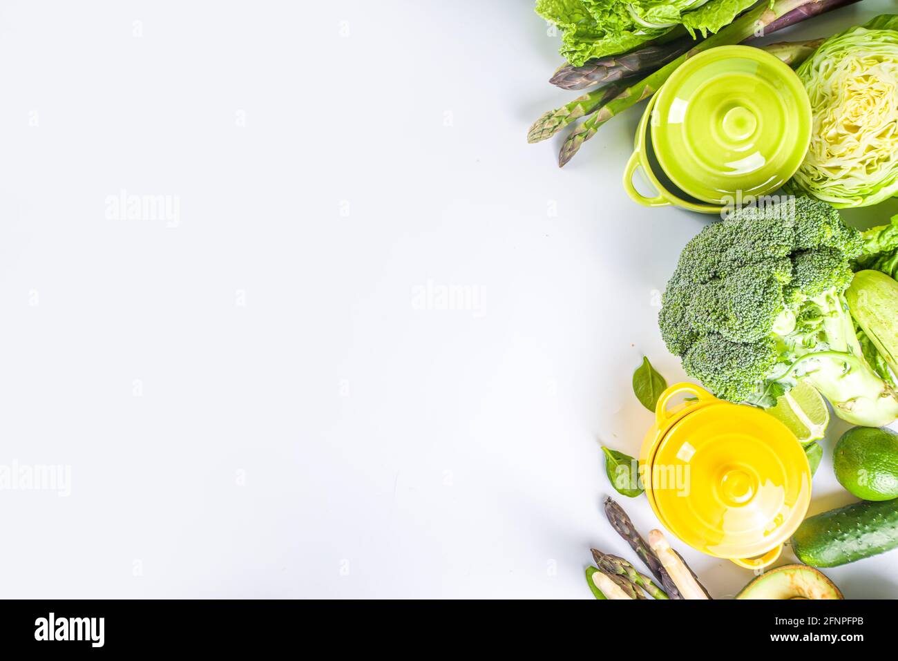Divers ingrédients biologiques de légumes de printemps verts avec pots de cuisson colorés vides sur table de cuisine blanche, vue du dessus. Soupe saine alimentation, ste Banque D'Images
