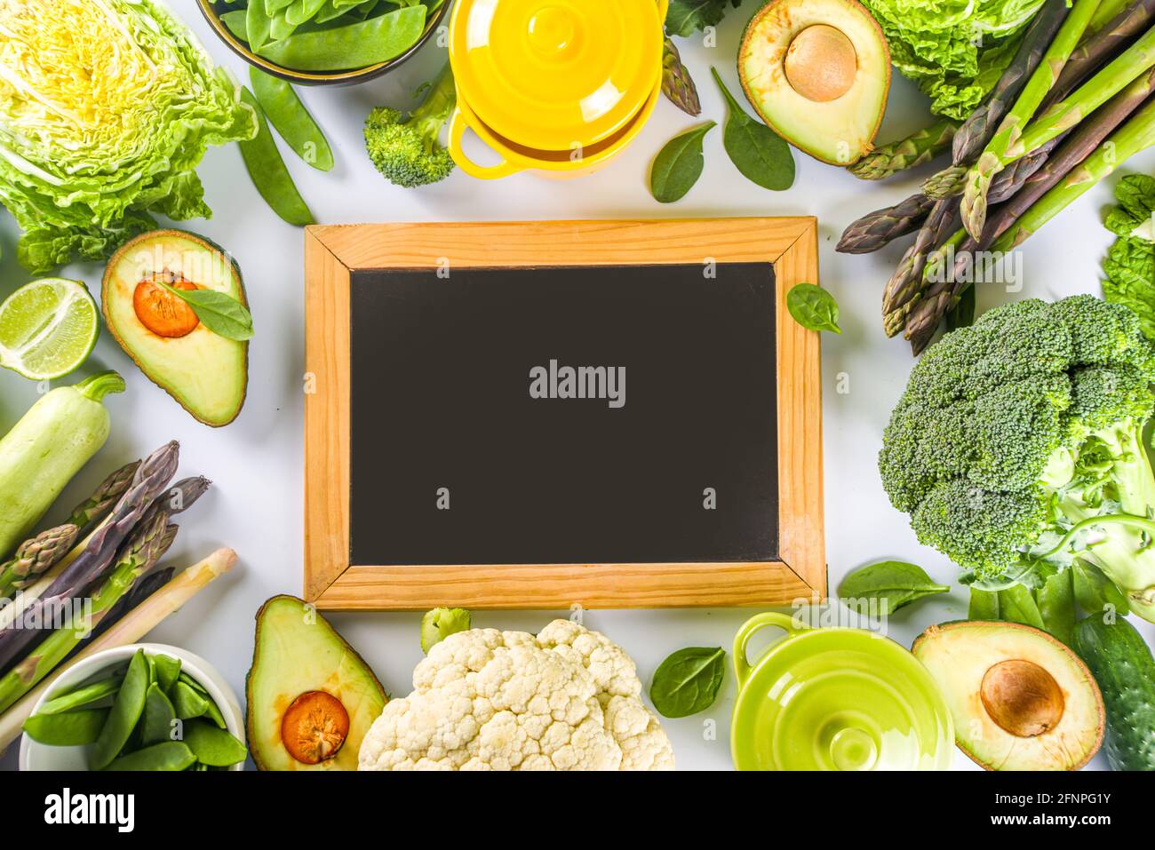 Divers ingrédients biologiques de légumes de printemps verts avec pots de cuisson colorés vides sur table de cuisine blanche, vue du dessus. Soupe saine alimentation, ste Banque D'Images