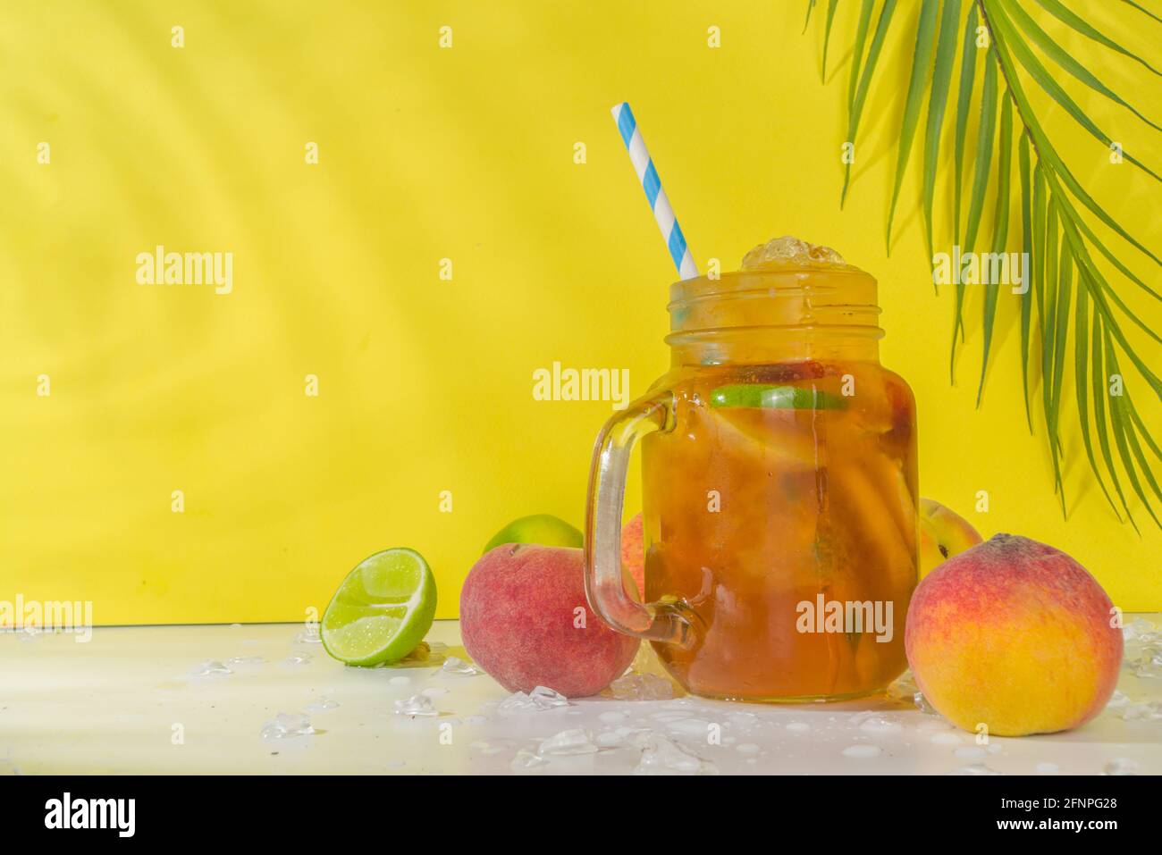 Boisson fraîche d'été, cocktail traditionnel de thé de pêche glacé avec glace pilée, tranches de pêche et citron, sur fond jaune ensoleillé et branché Banque D'Images