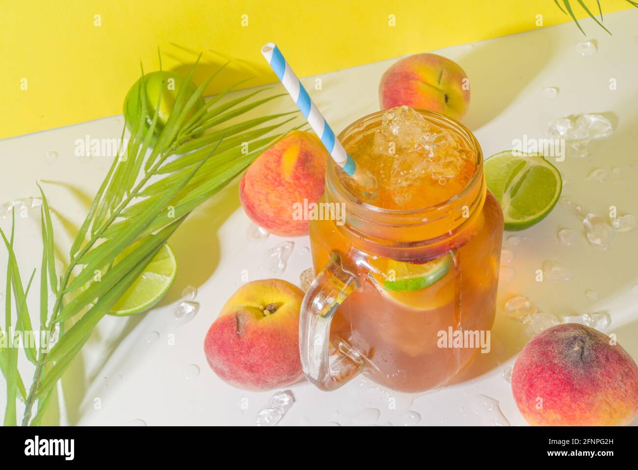 Boisson fraîche d'été, cocktail traditionnel de thé de pêche glacé avec glace pilée, tranches de pêche et citron, sur fond jaune ensoleillé et branché Banque D'Images