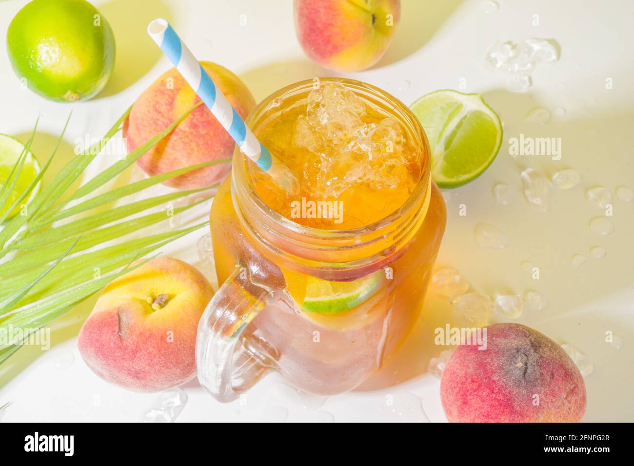 Boisson fraîche d'été, cocktail traditionnel de thé de pêche glacé avec glace pilée, tranches de pêche et citron, sur fond jaune ensoleillé et branché Banque D'Images
