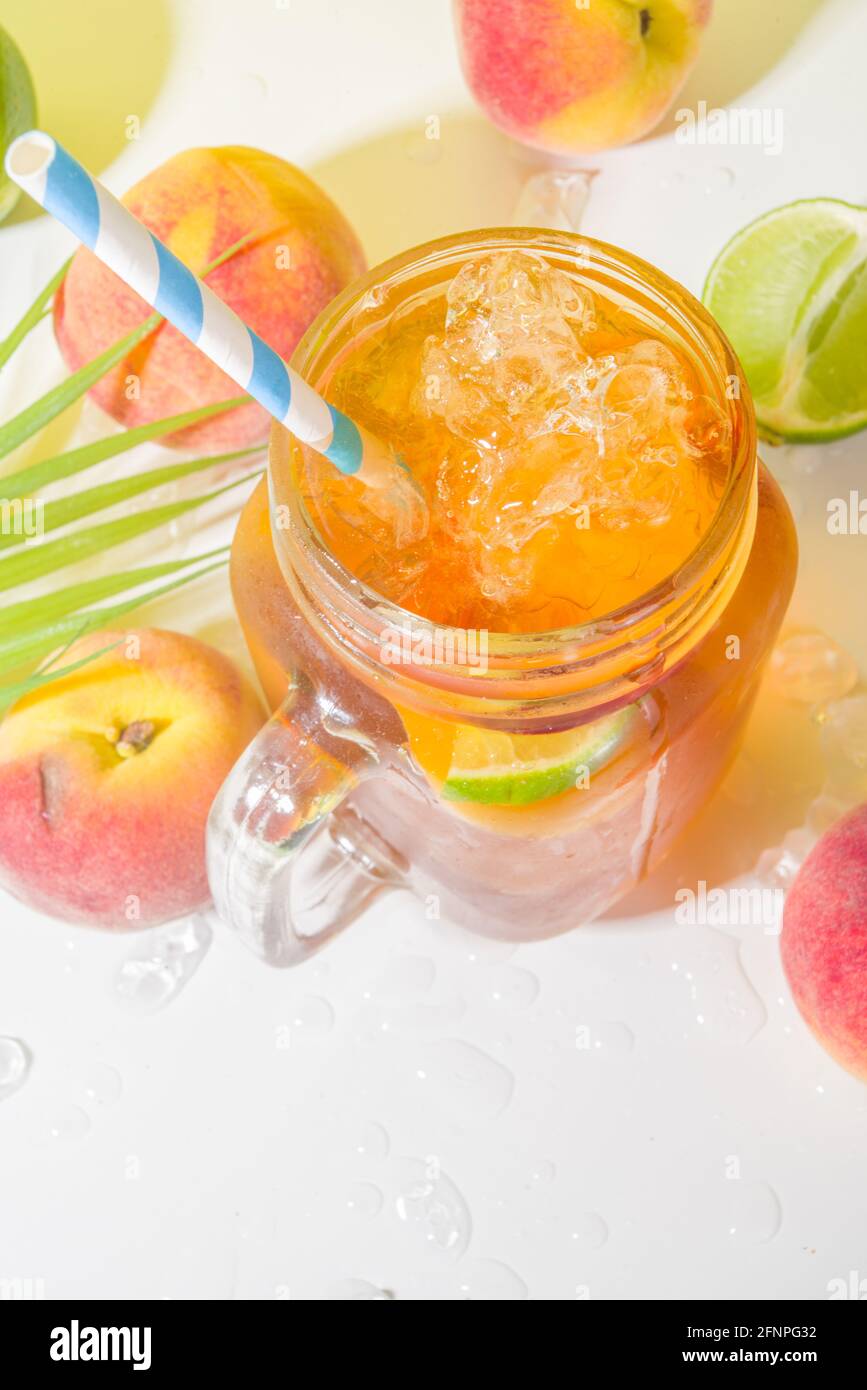 Boisson fraîche d'été, cocktail traditionnel de thé de pêche glacé avec glace pilée, tranches de pêche et citron, sur fond jaune ensoleillé et branché Banque D'Images