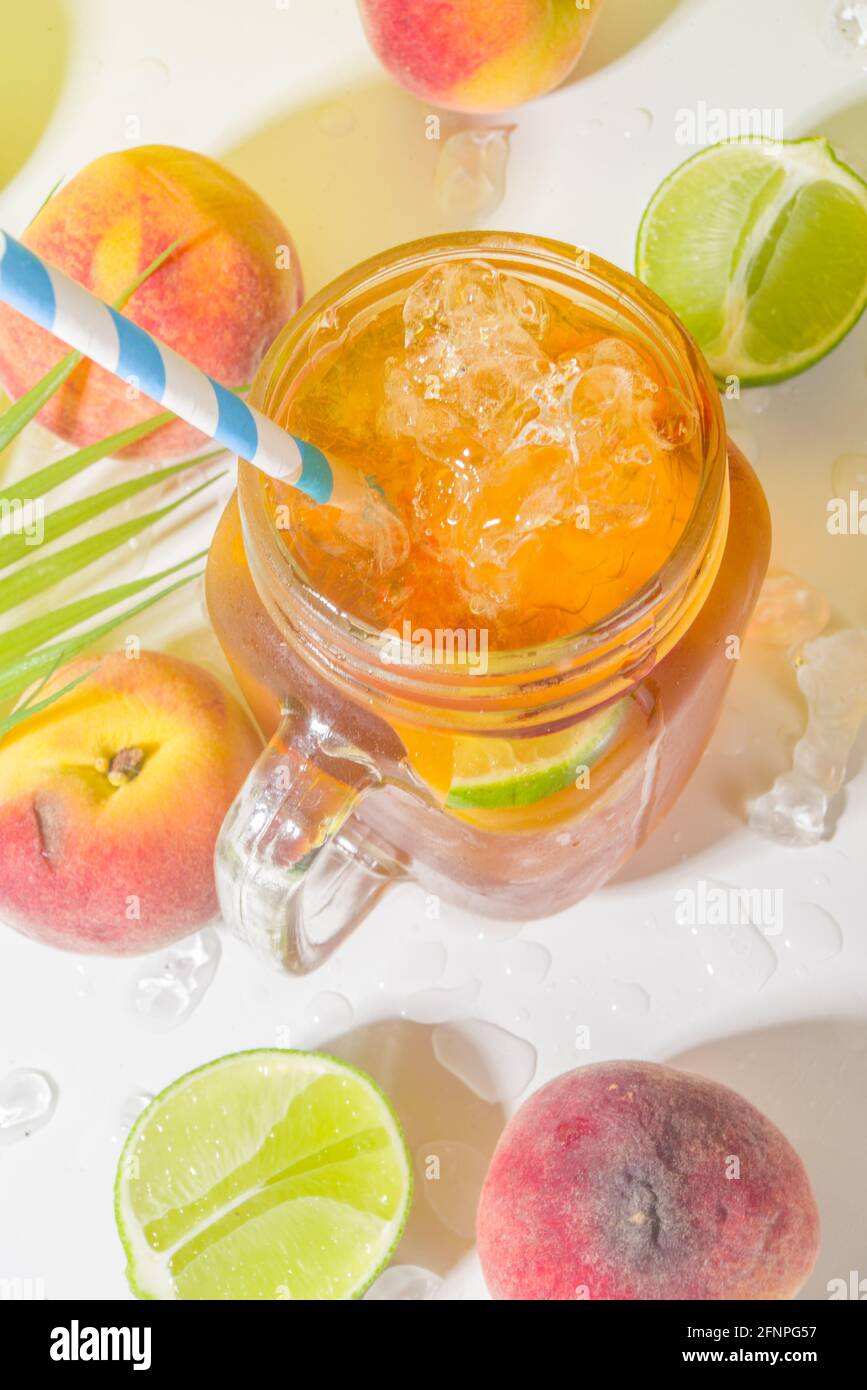 Boisson fraîche d'été, cocktail traditionnel de thé de pêche glacé avec glace pilée, tranches de pêche et citron, sur fond jaune ensoleillé et branché Banque D'Images
