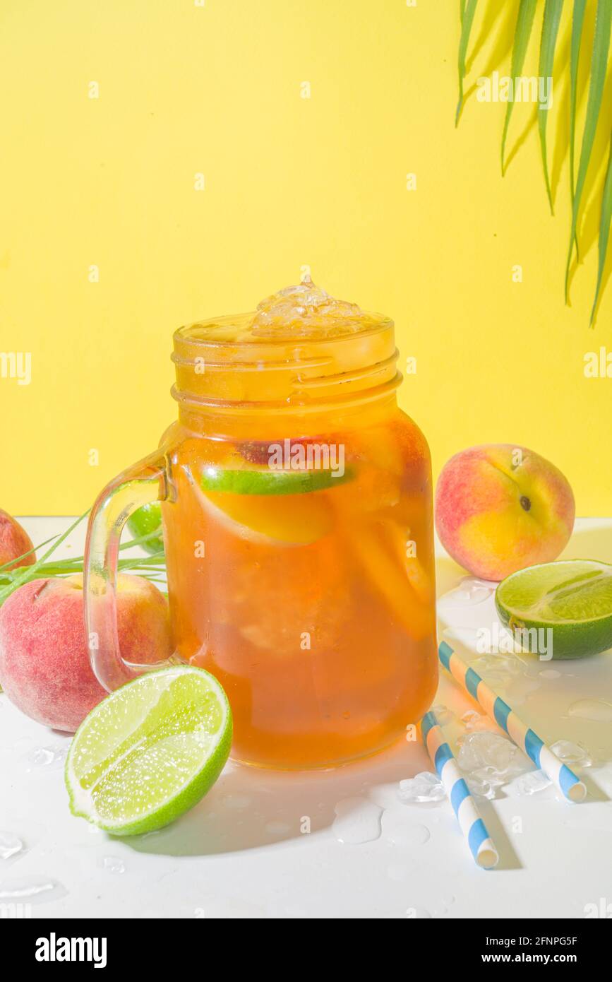 Boisson fraîche d'été, cocktail traditionnel de thé de pêche glacé avec glace pilée, tranches de pêche et citron, sur fond jaune ensoleillé et branché Banque D'Images