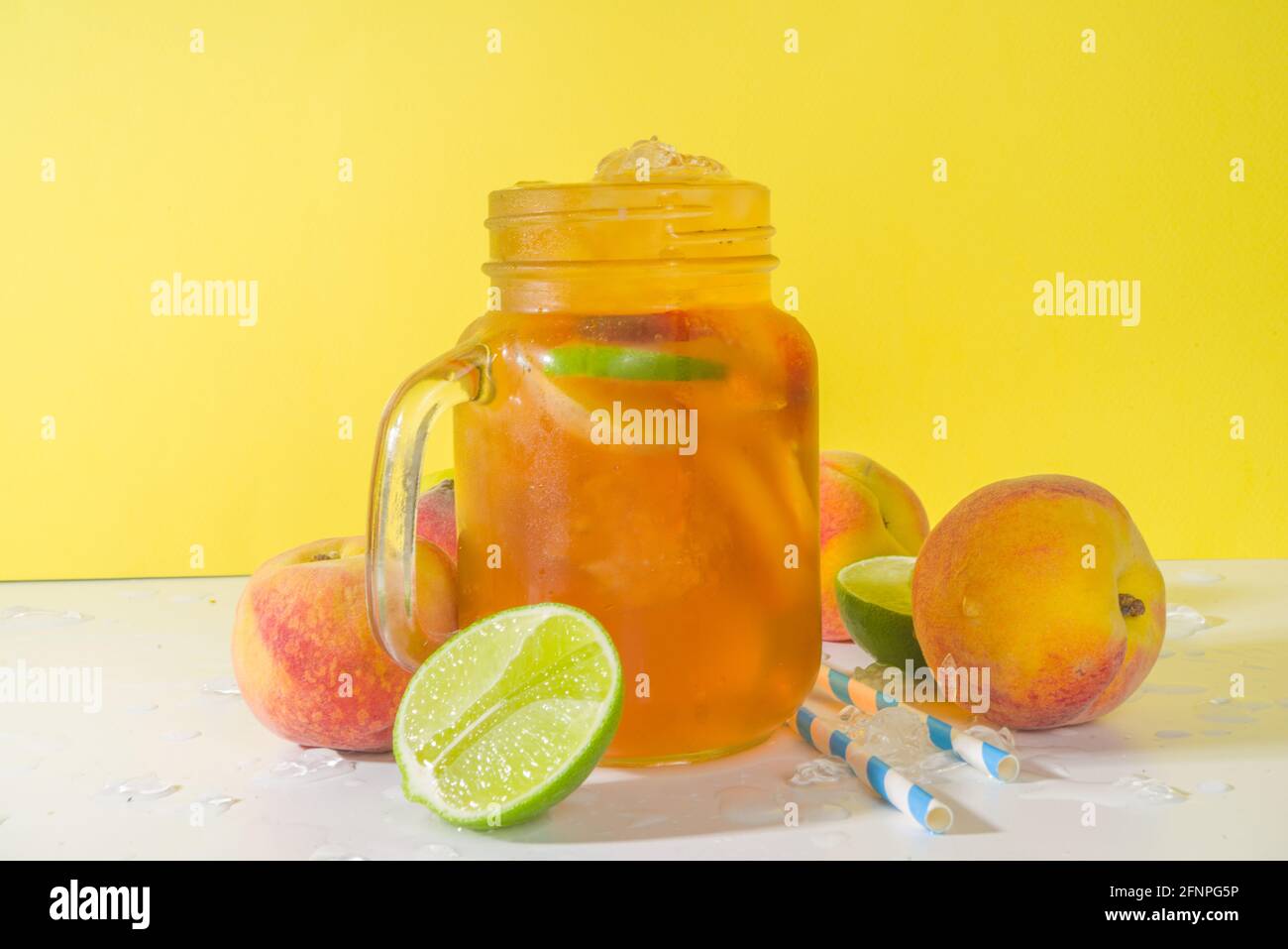 Boisson fraîche d'été, cocktail traditionnel de thé de pêche glacé avec glace pilée, tranches de pêche et citron, sur fond jaune ensoleillé et branché Banque D'Images