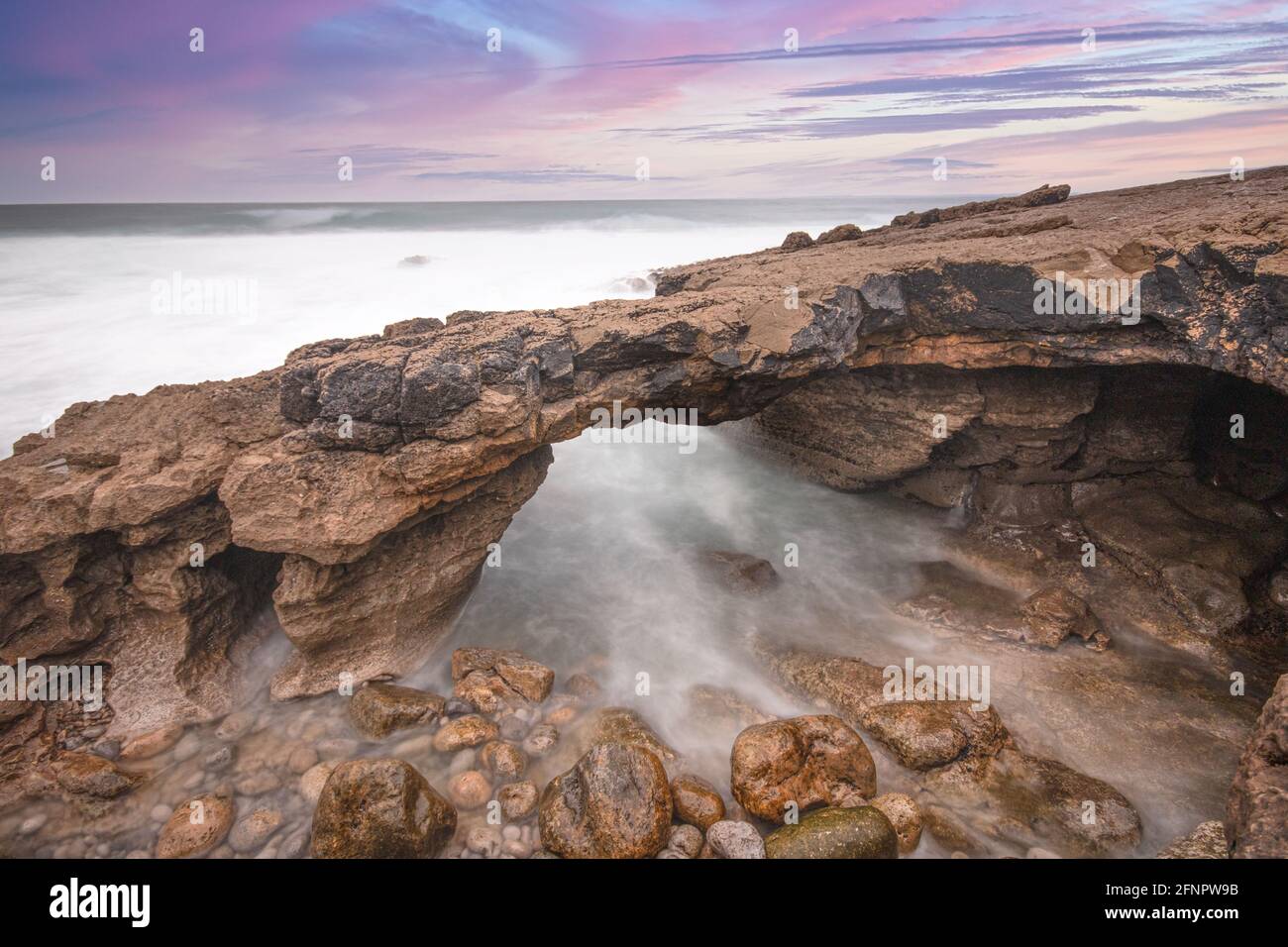 Formation rocheuse en forme d'arche sur la côte au coucher du soleil. Exposition longue Banque D'Images