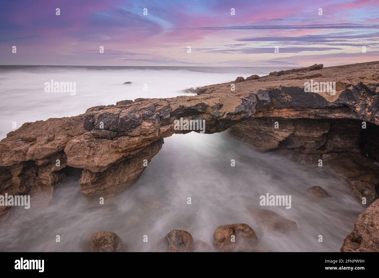 Formation rocheuse en forme d'arche sur la côte au coucher du soleil. Exposition longue Banque D'Images