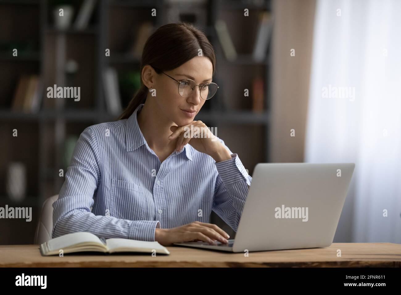 Jeune femme concentrée engagée dans un travail informatique au bureau à domicile Banque D'Images