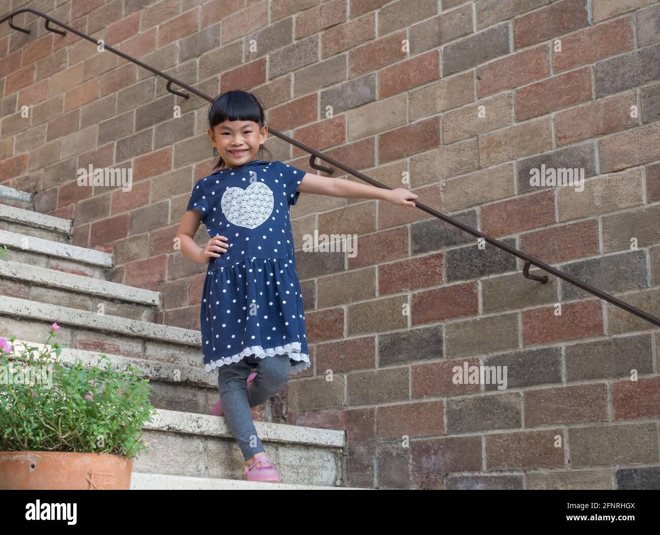 Petite fille asiatique posant au beau mur et à l'escalier. Banque D'Images