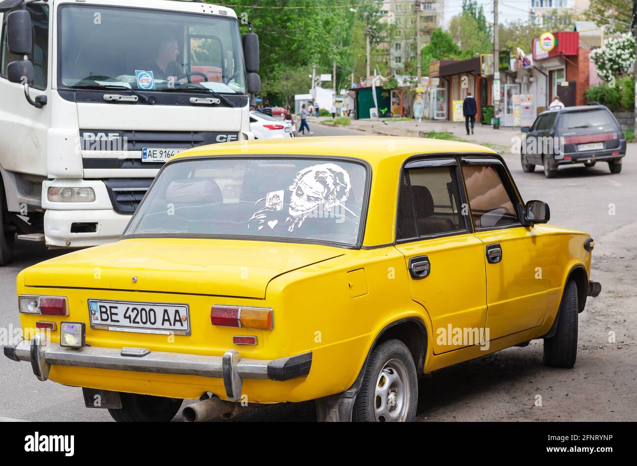 Vue arrière de la berline jaune avec le modèle Joker sur la lunette arrière. La voiture se trouve sur un parking. Un tracteur-remorque blanc passe à proximité Banque D'Images