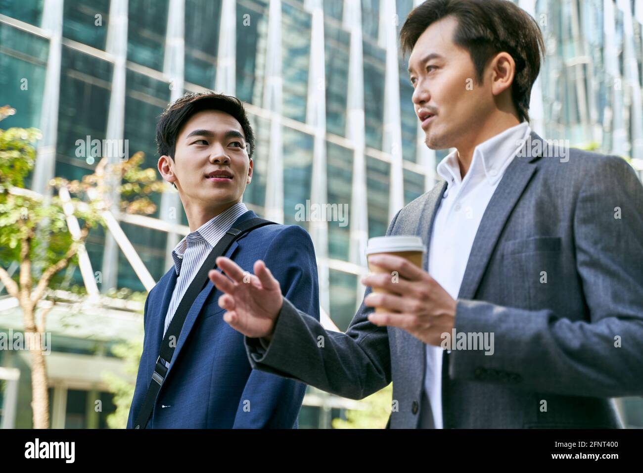 vue de côté de deux cadres d'entreprise asiatiques discutant des affaires pendant promenade dans la rue dans le centre-ville moderne Banque D'Images