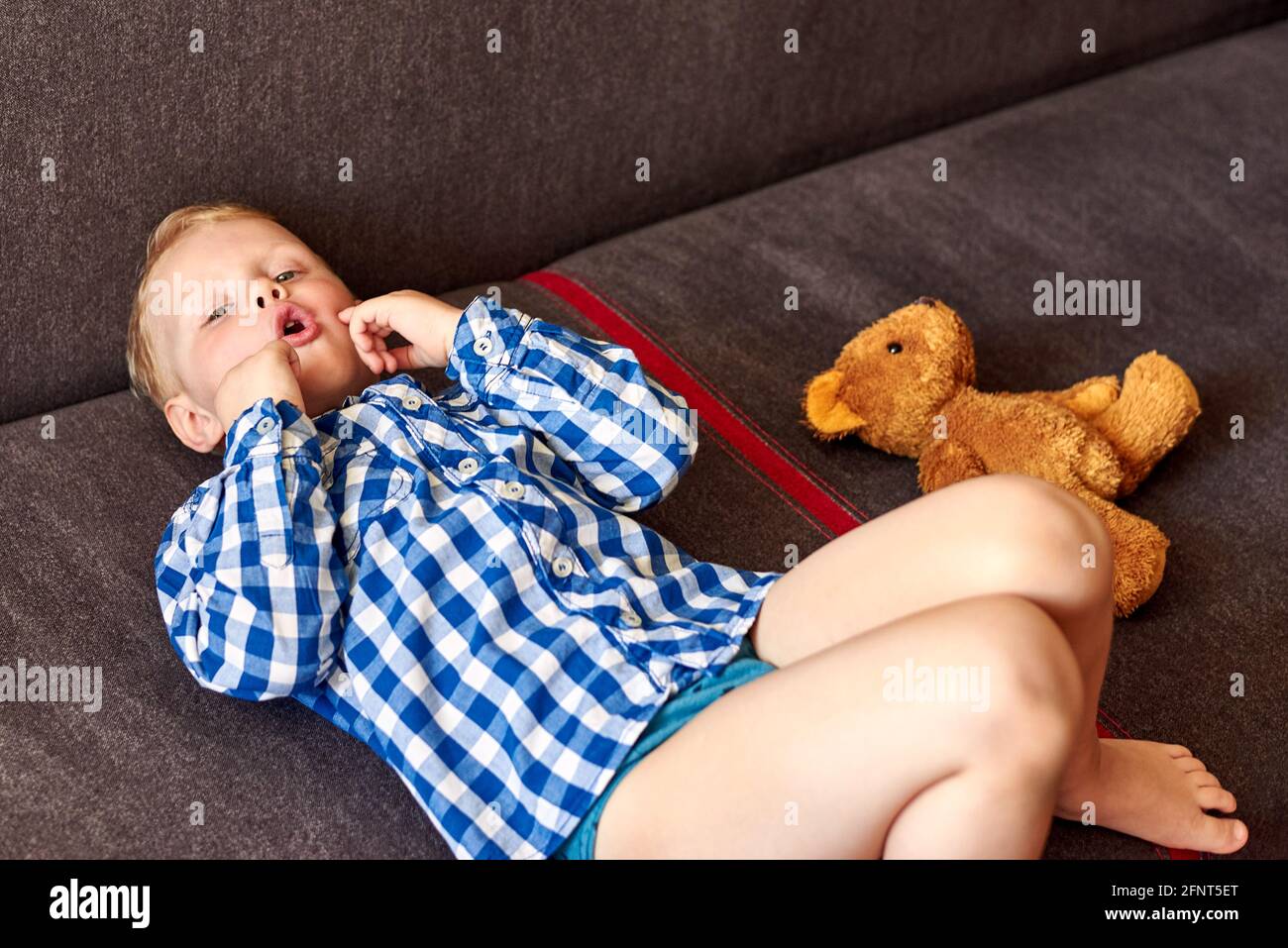 Un garçon de trois ans souffrant d'une déficience mentale se trouve sur le canapé près de l'ours en peluche à la maison. Banque D'Images