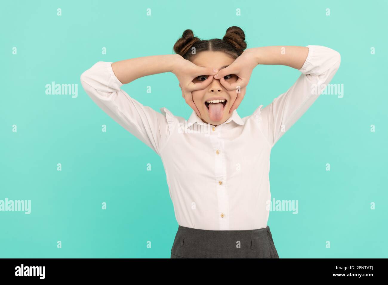 Heureux enfant d'âge scolaire faire des doigts masque super-héros collant la langue hors fond bleu, jouant Banque D'Images