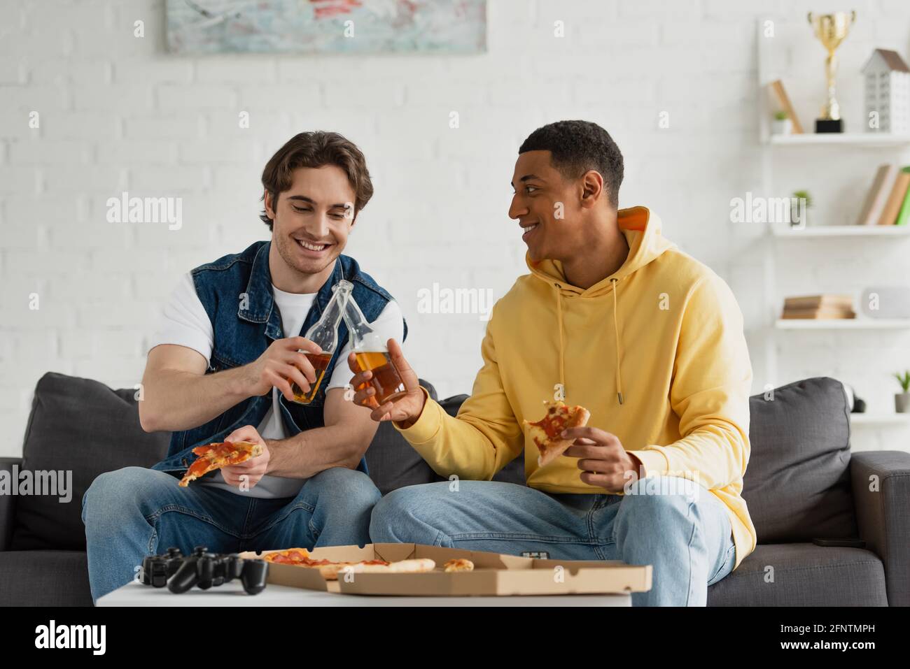 KIEV, UKRAINE - 22 MARS 2021: Des hipsters interraciaux se clinquant avec des bouteilles de bière sur le canapé dans le salon Banque D'Images